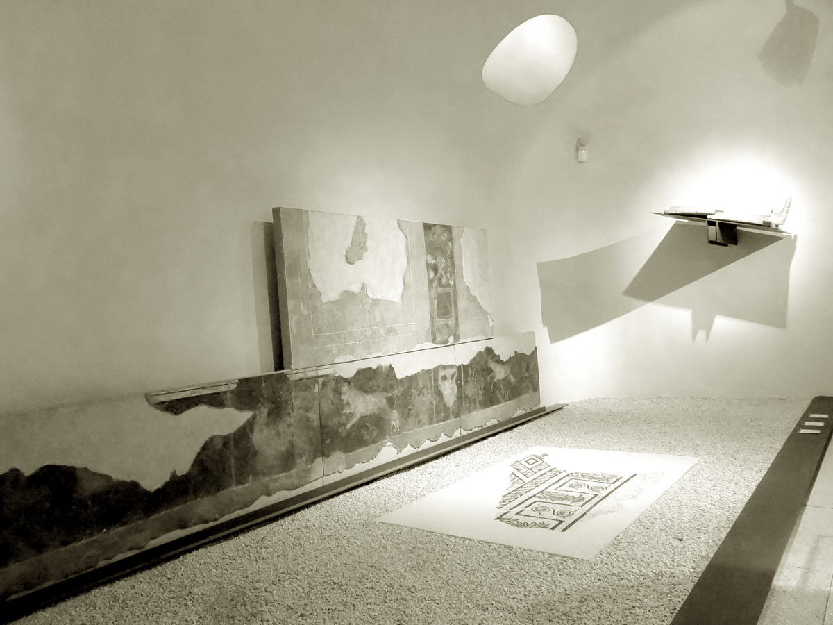 une salle de musée, des fragments de mosaïque, de fresque, un labyrinthe  sur le sol. Un bâtiment s'imagine sous le trou de lumière. 